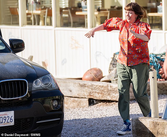 Olivia, 50, appeared in good spirits as she threw her arms in the air while wearing a red, silky shirt with detailed blue flowers and bananas