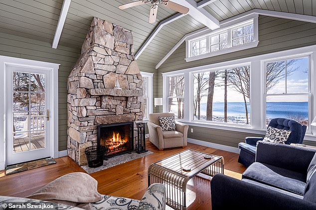 In the living room, a wide stone fireplace is surrounded by an abundance of natural light, exposed ceiling beams and beautiful hardwood floors