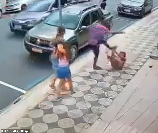 A man kicks at a woman as she lies on the ground after she punched a young girl in the face without being provoked