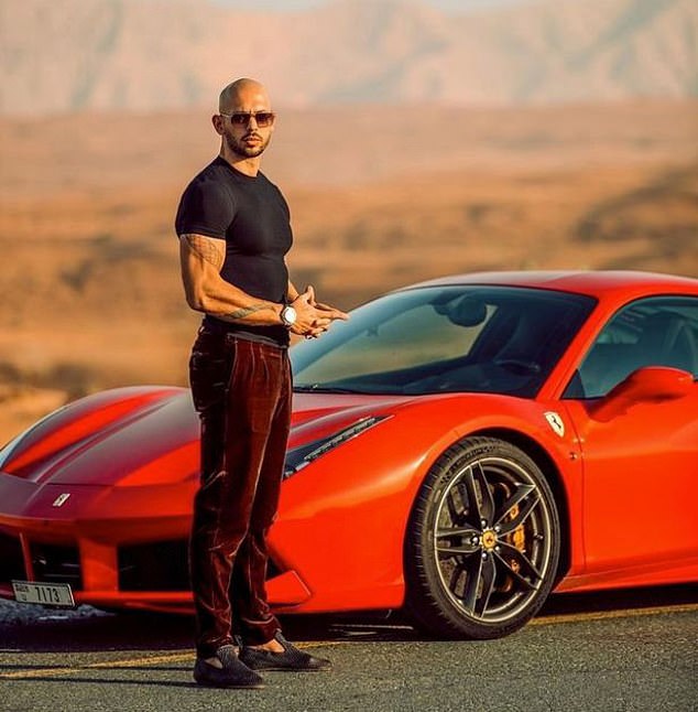 Tate does the hand gesture again as he poses in front of a luxurious red Ferrari