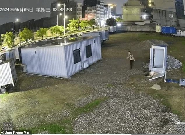 The man walks out of the portaloo onto the grass, while the woman is still on the ground