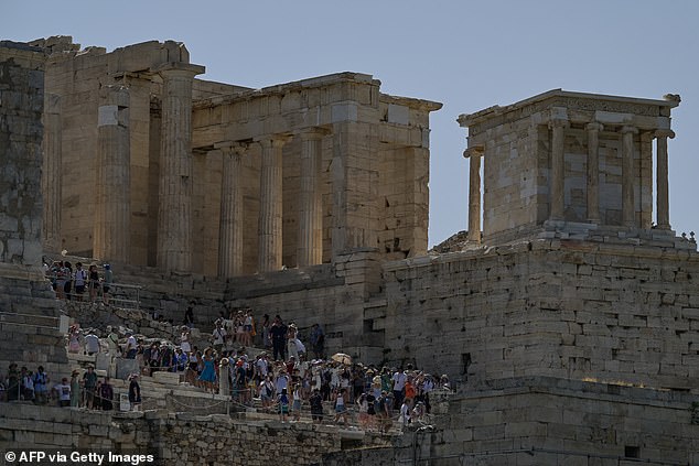 Tourists sit on the steps of the ancient Acropolis Hill during a hot day in Athens, Greece