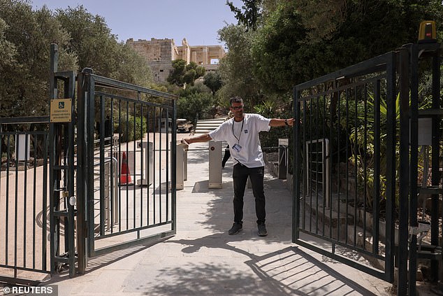 A worker closes the exit door of the Acropolis archaeological site as it temporarily closes due to a heat wave hitting the country