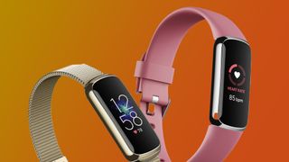 Two Fitbit fitness trackers on an orange background
