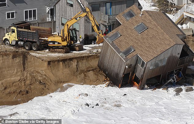 Construction equipment prepares to demolish a house that fell off its foundation after yesterday's winter storm eroded the shoreline on Plum Island.