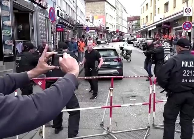 The man dressed in black wields an ax and holds a firebomb near the Reppenbahm, in Hamburg, as he shouts at officers standing behind a barrier.