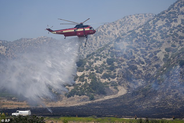 A helicopter drops water as firefighters clean up after the Post Fire rips through