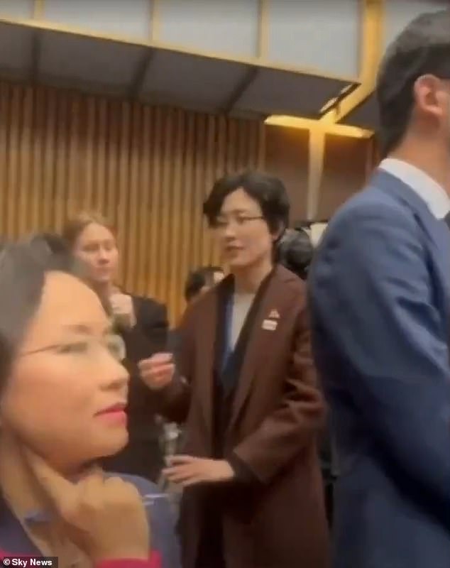 Cheng Lei is seen (left) with a Chinese official standing nearby in an attempt to block her view