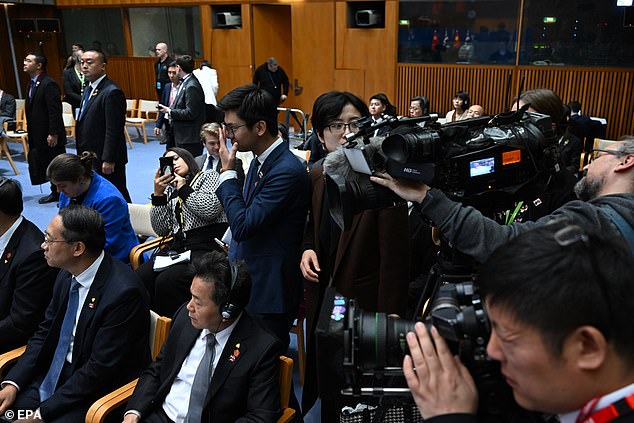 Two Chinese embassy officials (center) standing between cameras and Lei (sitting behind them, not visible)