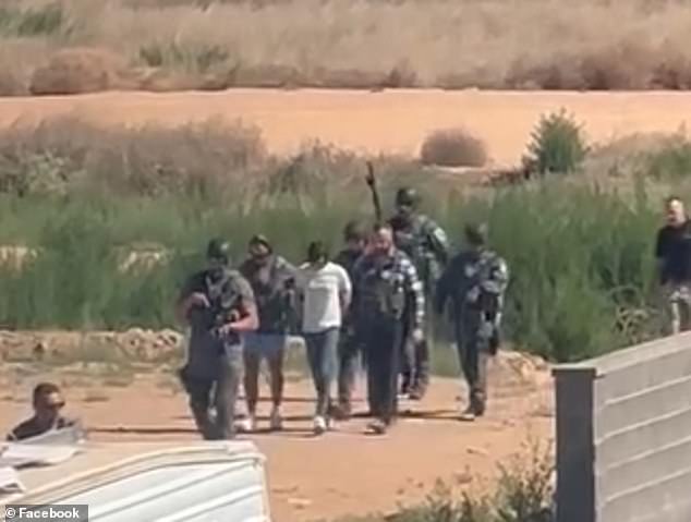 Flanked by seven officers, some of whom are in tactical gear and carrying assault rifles and a dog, Bailey is led out of a desert area as two men hold her down.