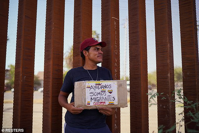Colombian migrant David Laguada holds a sign "Help us, we are migrants" as he waits with his family for a CBP One appointment to reach the United States next to the border wall during a heat wave in Mexicali, Mexico