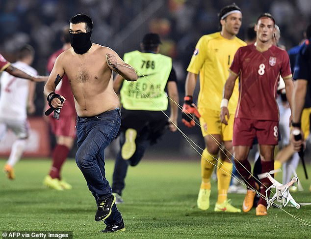 A masked Serbian supporter makes off with the drone carrying the controversial flag as players watch in the background