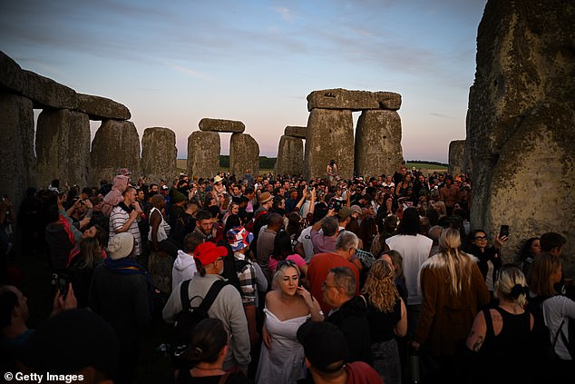 Hundreds of people gather in the stones, including families with young children on their shoulders