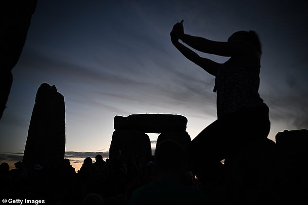 A woman takes a photo while sitting on a friend's shoulders at Stonehenge