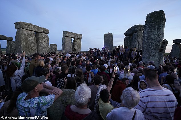 People gather at Stonehenge in Wiltshire at sunset as they wait to welcome in the summer solstice