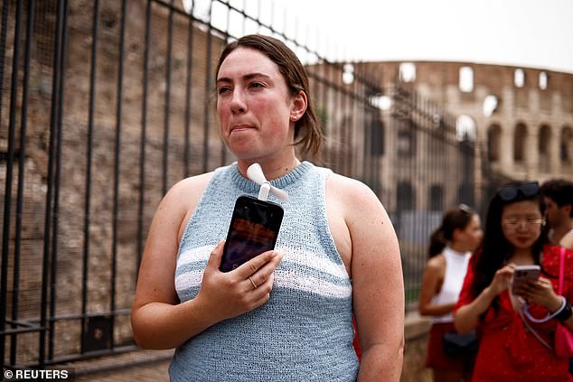 Claira from Massachusetts uses a fan attached to her iPhone to cool down as she waits in line to enter the Roman Forum