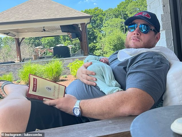 The Grammy nominee is on daddy duty as he reads a book with one hand while holding Beau in his other arm