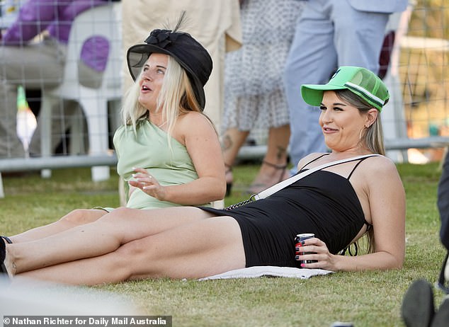 Two friends are seen spending some time on the grass during the horse racing