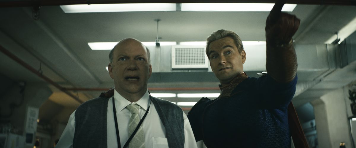 Homelander, his arm around a terrified scientist, points to something off-screen in a scene from season 4 of The Boys.