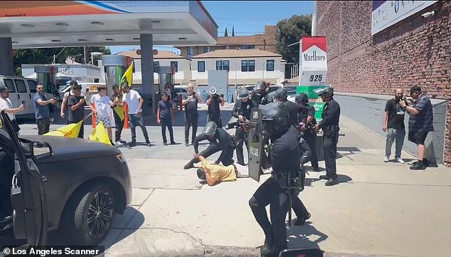 Another mask-wearing protester in a yellow shirt was detained outside the vehicle