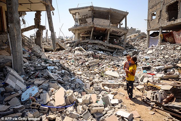 A woman stands with a child in her arms, surrounded by the rubble of buildings destroyed during the Israeli bombardment of Khan Yunis in the southern Gaza Strip on June 23, 2024