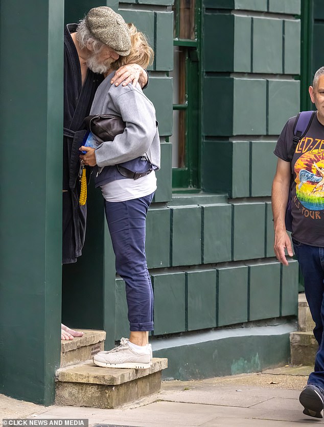 A man walks past as Sir Ian McKellen greets a friend outside his London home yesterday