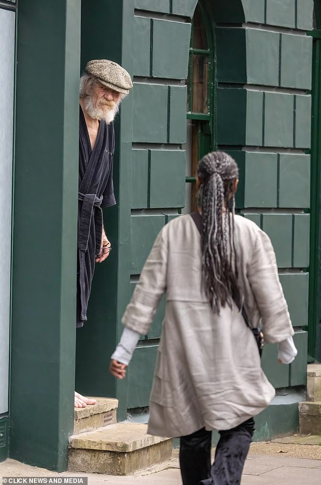 A woman walks past as Sir Ian McKellen looks out from his home in London yesterday