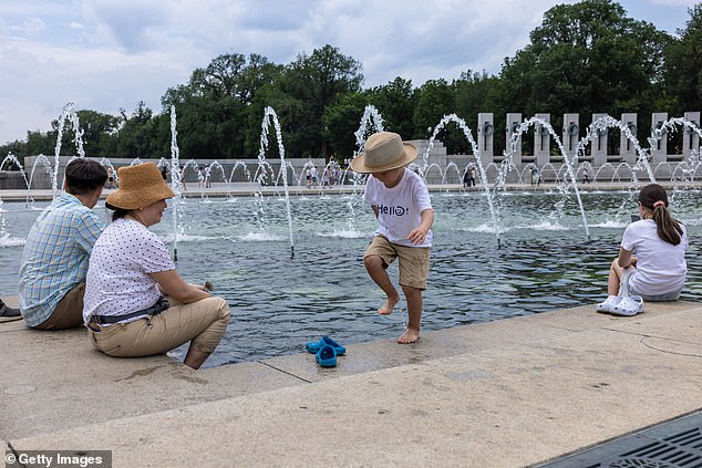 People sit with their feet in the fountain at the WWII memorial amid a heat wave