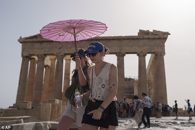 Tourists with an umbrella walk in front of the Parthenon on the ancient Acropolis in the center of Athens, Wednesday, June 12, 2024