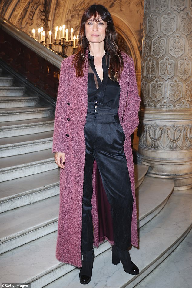 Caroline de Maigret wore a burgundy long coat over a black satin jumpsuit and boots with thick heels