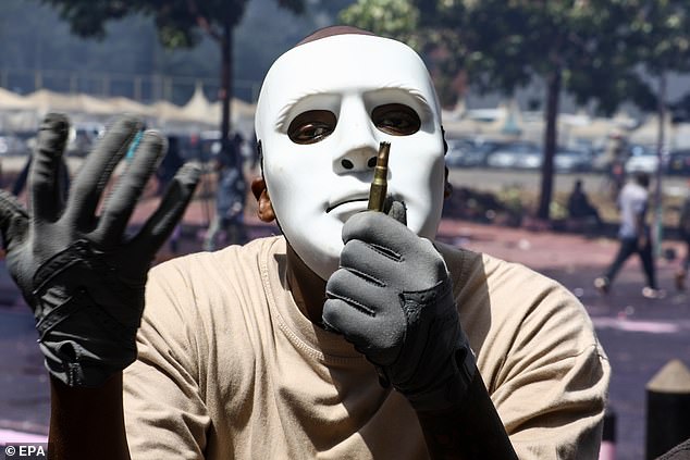 A masked protester holds an empty ammunition shell used by police during a protest against proposed tax increases