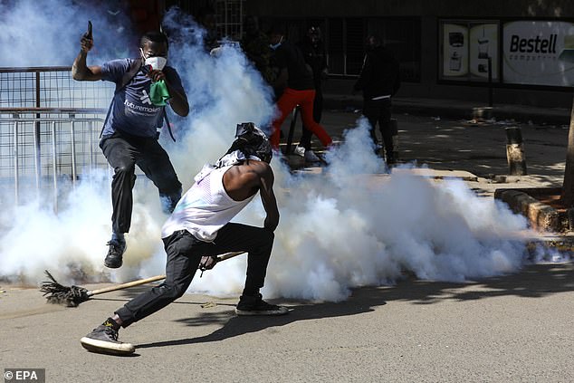 A protester uses a broom to fend off a tear gas canister