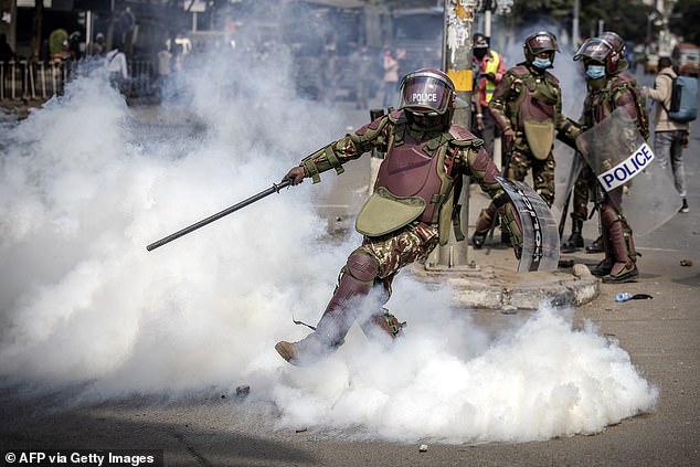 A Kenyan police officer kicks a tear gas canister during a nationwide strike in protest against tax increases