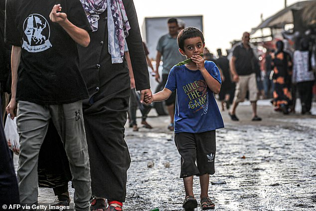 A boy eats a piece of watermelon as he walks with a woman along a market street in Deir el-Balah in the central Gaza Strip on June 27, 2024