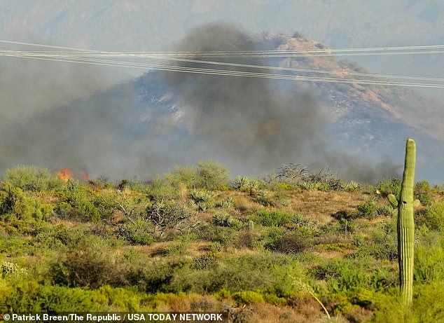 Fire peaks over a hill as smoke rises from the Boulder View fire in north Scottsdale