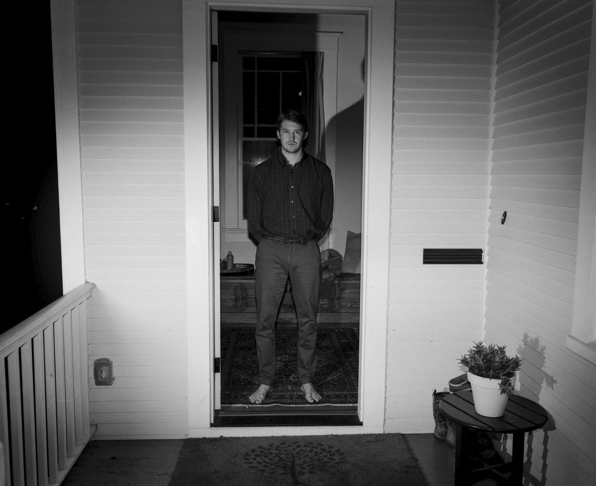 Joe Alwyn, photographed barefoot and in black and white, stands in the doorway of a house in Kinds of Kindness