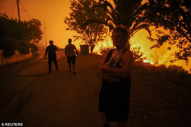 A local resident holds bottles of water next to a forest fire in the village of Latas, southern Greece, June 21, 2024