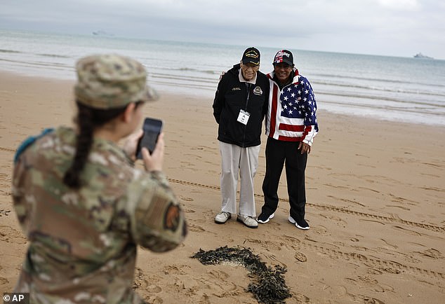 An American soldier takes a photo of American WWII veteran Sid Edson, center left, during a ceremony on Omaha Beach