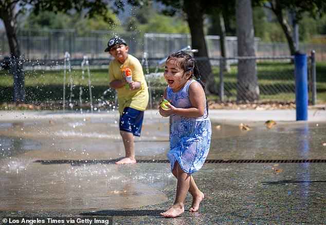 A four-year-old child runs through a splash pool to cool off while another child sprays her amid the heat at Rio de Los Angeles State Park in Los Angeles