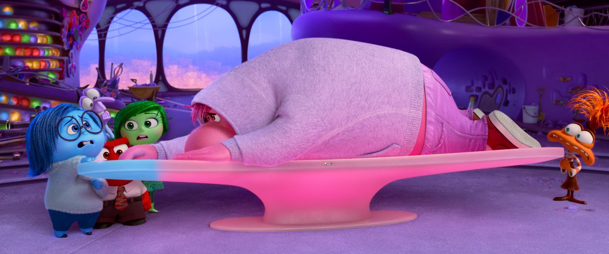 Shyness, a big, blobby, pink guy in a gray hoodie, lies sprawled over the control panel in the Emotions Headquarters as the other characters stand around worriedly in Pixar Animation Studios' Inside Out 2