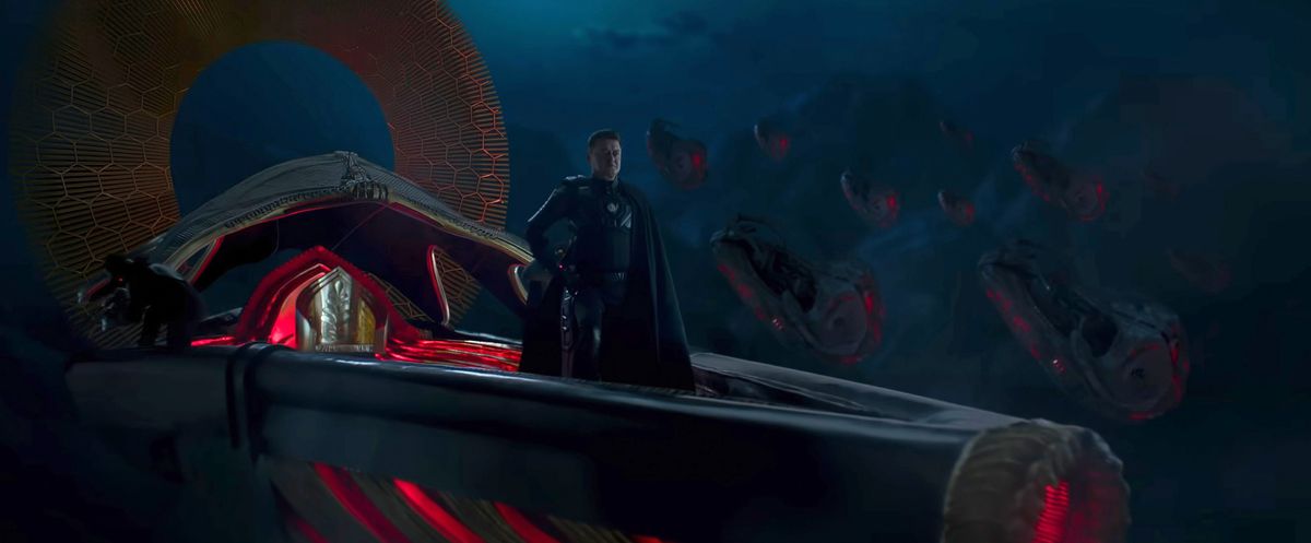 In a promotional photo for the Indian sci-fi blockbuster Kalki 2989 AD, a man in black clothing and a long black cape stands in a dark, V-shaped object that looks like a single spaceship with a crimson interior and closing crimson accents.  Behind him in the darkness, a group of similar-looking ships glow against the dark mountains.