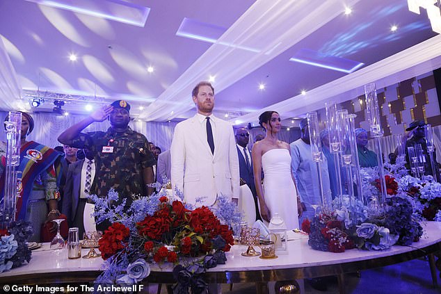 Prince Harry and Meghan Markle stand in front of God Save The King in Abuja, Nigeria at an event with Nigeria Unconquered