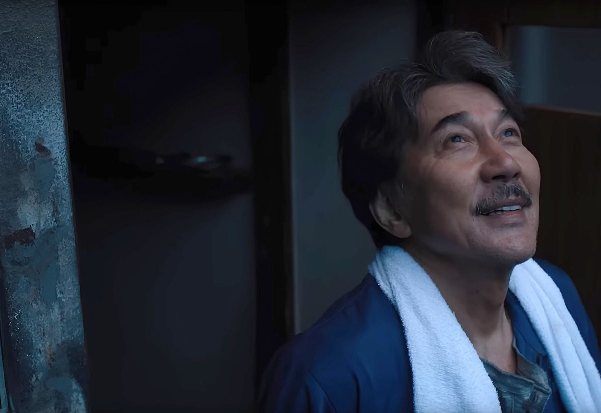 A middle-aged Japanese man looking up at the sky, smiling.  He has a towel draped around his shoulders.