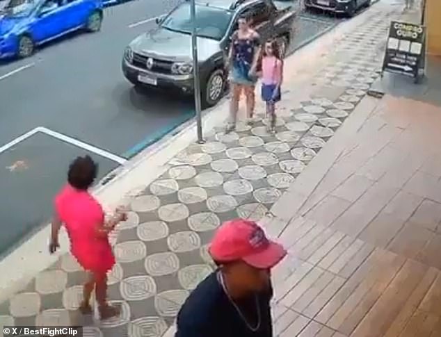 A woman (left) was seen approaching a family on a Brazilian sidewalk before punching a child in the face