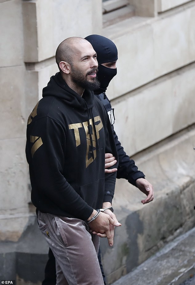 Former professional kickboxer and influencer Andrew Tate gestures with his hands while being escorted in handcuffs in Romania