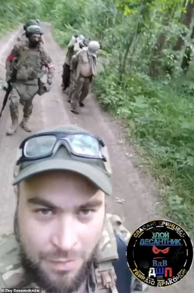 Russian soldier takes selfie with Ukrainian war prisoners, who can be seen blindfolded in the background