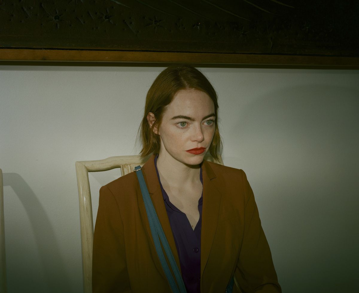 Emma Stone sits in a chair, with a dark light, looking worried, with short red hair and scarlet lipstick, in Kinds of Kindness