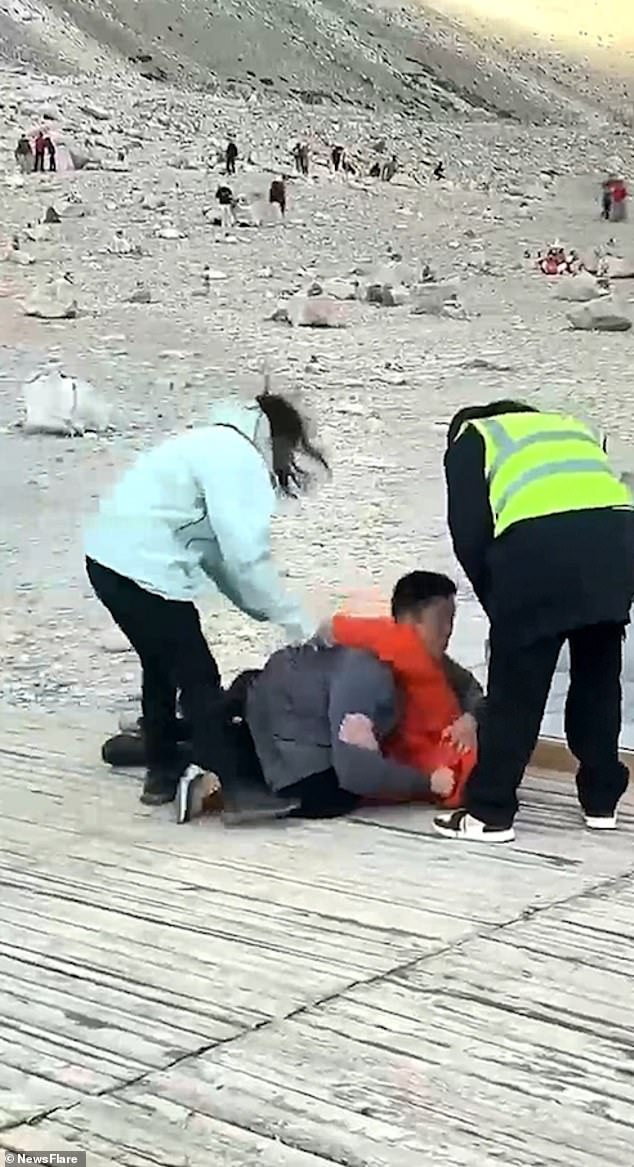 The woman in the light blue coat tries to pull one of the men away