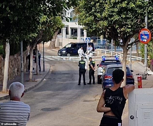 Mr Grant, a physiotherapist from Waterford, was found unconscious at around 4.30am near Magaluf's infamous Punta Bellena strip, which is full of late-night bars, nightclubs and lap dancing spots.  Pictured: Local residents watch today as police work on the scene