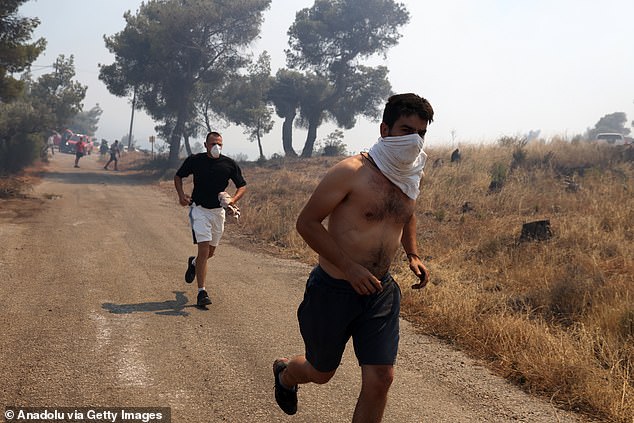 KERATEA -- People cover their faces while running away from a forest fire